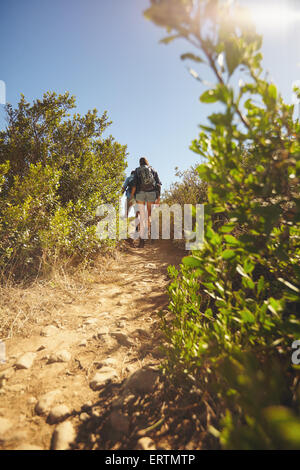 Image des personnes marchant à travers piste de montagne. Vue arrière shot of couple hiking sur chemin de terre par de l'herbe et des plantes sur mountai Banque D'Images