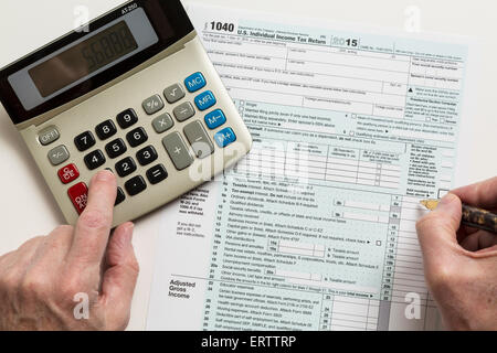 Man filling in USA Formulaire d'impôt 1040 pour l'année 2015 avec la calculatrice Banque D'Images