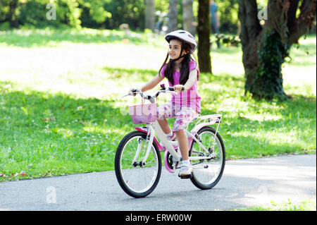 Petite fille dans un quartier branché tenue rose rose avec Vélo et casque à bicyclette Équitation Banque D'Images