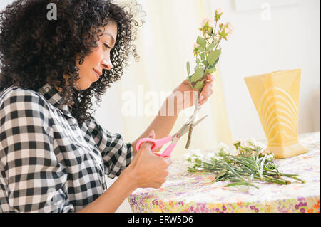 Mixed Race woman cutting tiges florales à table Banque D'Images