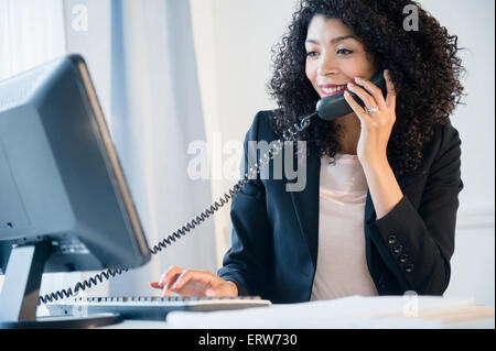 Mixed Race businesswoman using computer in office et téléphone Banque D'Images