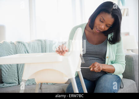 Femme enceinte noir assemblage chaise haute dans la salle de séjour Banque D'Images