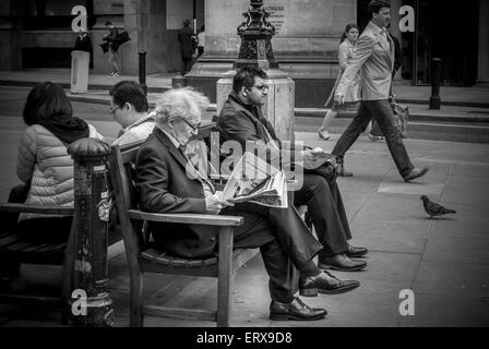 Businessman assis sur un banc à l'extérieur la lecture de journal, Londres, Royaume-Uni. Banque D'Images