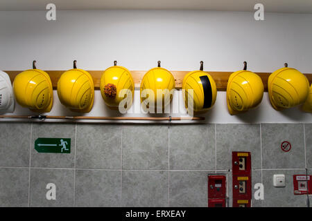 Chapeaux de construction jaune accroché sur un rack, l'un d'eux a une bordure sur elle Banque D'Images