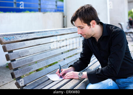 L'homme écrit lettre sur un banc Banque D'Images