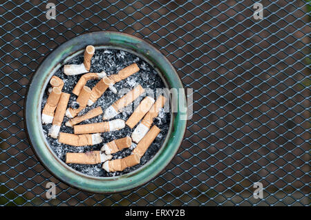 Un cendrier plein de mégots sur un treillis métallique table, photographié d'en haut Banque D'Images