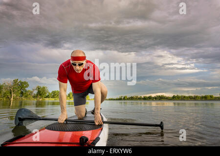 Senior male paddler commencer son entraînement sur stand up paddleboard, un lac local dans le Colorado sous ciel nuageux Banque D'Images