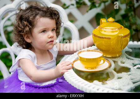 Jolie petite fille assise dans jardin avec théière et tasse Banque D'Images