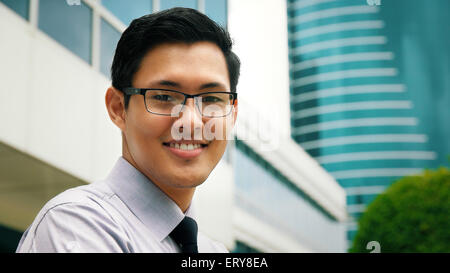 Portrait de heureux et confiant young asian woman. L'homme se trouve dans une rue contre les immeubles de bureaux et les croix armoiries lo Banque D'Images