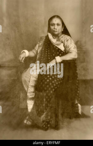 Vieux vintage antique 1900s noir et blanc studio photographie de femme indienne portant une saree assis dans une chaise , inde , asie Banque D'Images