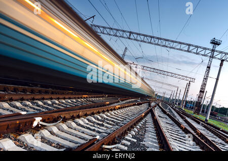 Le train de voyageurs à grande vitesse sur pistes avec l'effet de flou au coucher du soleil. Gare ferroviaire de l'Ukraine Banque D'Images