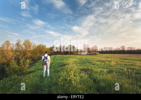 Beau coucher du soleil. Paysage de printemps avec l'homme sur le terrain. Arbres, ciel bleu et nuages Banque D'Images