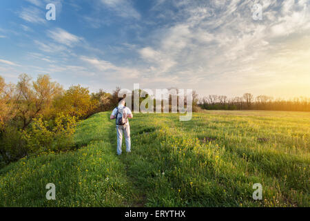 Beau coucher du soleil. Paysage de printemps avec l'homme sur le terrain. Arbres, ciel bleu et nuages Banque D'Images