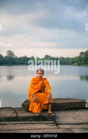 SIEM REAP, Cambodge - 30 octobre 2014 : Novice moine en robe orange se trouve le long de la douve près de l'entrée à Angkor Wat. Banque D'Images