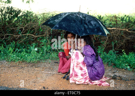 Mère et fille avec chèvre assis sous le parapluie sous la pluie, Tamil Nadu ; Inde, asie Banque D'Images