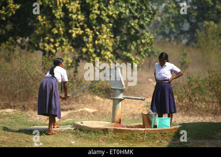 Enfants d'école filles dans l'uniforme scolaire tirant l'eau de la pompe manuelle à Jharkhet ; Inde Banque D'Images