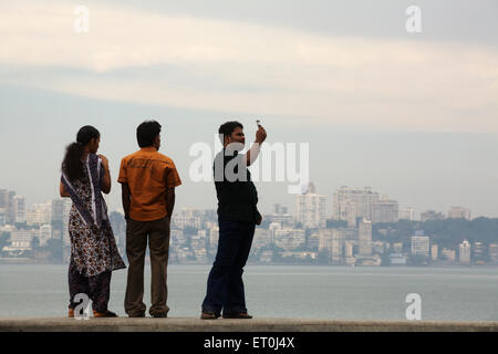 Couple standing alors que l'un des jeunes est la prise de photos de Marine Drive ; Bombay Mumbai Maharashtra ; Inde ; Banque D'Images