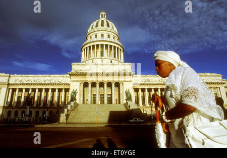 Santera femme passant le Capitolio Nacional, La Havane, Cuba. Santería, également connu sous le nom de Regla de Ochá ou la regla de Lucumí est une religion syncrétique d'origine caraïbe qui s'est développé dans l'Empire espagnol entre les esclaves de l'Afrique de l'Ouest. Santería est influencée par et fusionnés avec le Catholicisme Romain. Sa langue liturgique, un dialecte de Yoruba, est également connu comme Lucumí. Banque D'Images