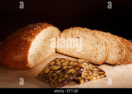 Tranches de pain de grains entiers sur planche à découper en bois avec du fromage sur fond noir. Banque D'Images