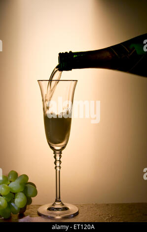 Silhouette de bouteille de champagne verser dans la flûte de champagne de style. Raisins verts frais à côté d'un verre de vin. Banque D'Images