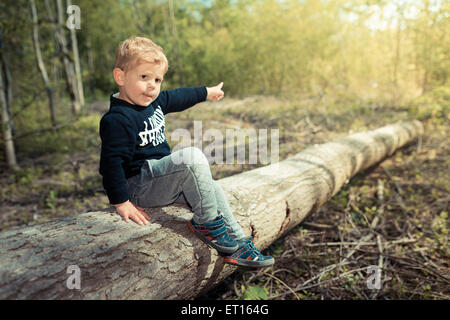 Petit garçon enfant couché sur un arbre coupé explorer la nature Banque D'Images