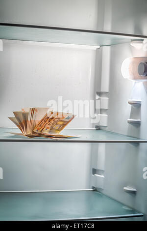 De l'argent frais dans le réfrigérateur : une poignée de billets de 50 euros éclairé par la lumière froide d'un réfrigérateur vide Banque D'Images