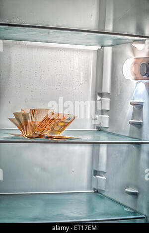 De l'argent frais dans le réfrigérateur : une poignée de billets de 50 euros éclairé par la lumière froide d'un réfrigérateur vide Banque D'Images