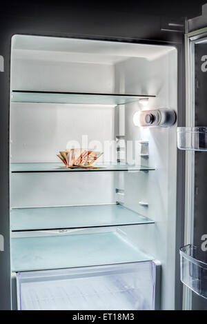 De l'argent frais dans le réfrigérateur : une poignée de billets de 50 euros éclairé par la lumière froide d'un réfrigérateur vide Banque D'Images