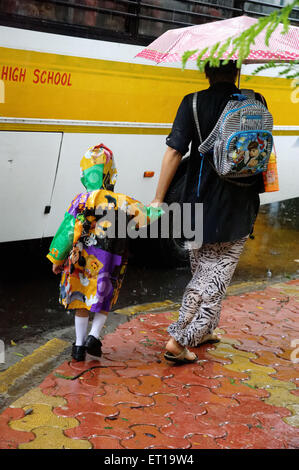 Mère avec parapluie garçon marche dans l'imperméable de bus scolaire à la pluie de mousson en Inde - M.# 364 Banque D'Images