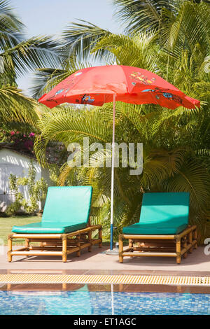 Couleur rouge unique parasol près de la piscine de l'eau bleu palmiers vert et bleu ciel ; Palolem beach Goa ; Inde ; Banque D'Images