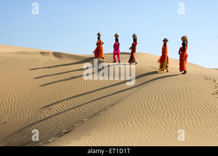 Les femmes avec des pots en terre sur la tête en marchant sur désert de khuhri ; ; ; Inde Rajasthan Jaisalmer Banque D'Images