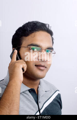 Jeune homme à l'aide d'un téléphone mobile et souriant ; Inde M.# 556 Banque D'Images
