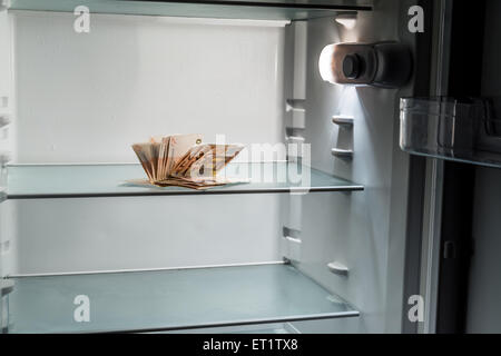 De l'argent frais dans le réfrigérateur : une poignée de billets de 50 euros éclairé par la lumière froide d'un réfrigérateur vide Banque D'Images