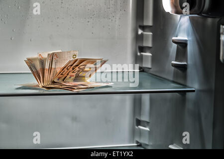 De l'argent frais dans le réfrigérateur : une poignée de billets de 50 euros éclairé par la lumière froide d'un réfrigérateur vide Banque D'Images