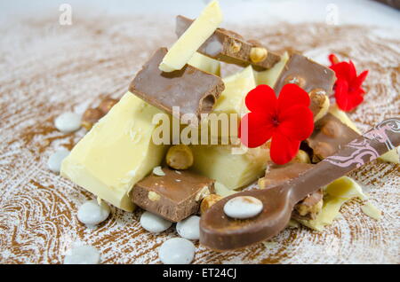 Cubes de chocolat noir et blanc sur une table saupoudrée de cacao décorées de fleurs et une cuillère de chocolat Banque D'Images