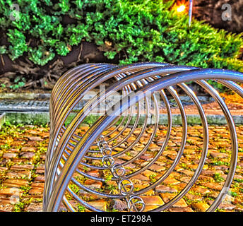 Cercle d'acier pour les vélos stationnement à Prague le sol en brique orange brunâtre avec des brins d'herbe verte et le musc. Arbres en arrière-plan Banque D'Images