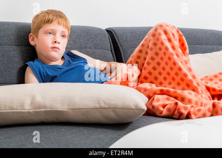 Les jeunes, triste, red haired boy de sept se prélasser sur le canapé à l'intérieur Banque D'Images