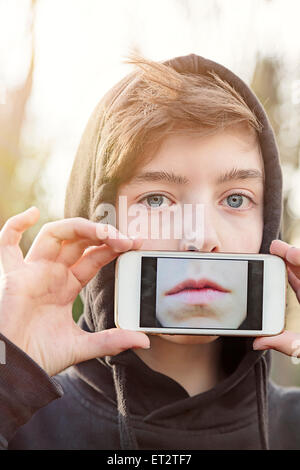 Virtual immo, teenage boy holding a smart phone en face de son visage Banque D'Images