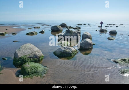 Femme marche dans l'eau dans la plage de sable de paysage surréaliste avec de petites roches. Banque D'Images