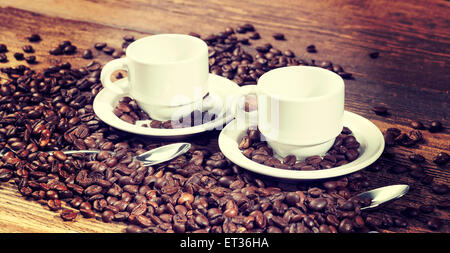 Vintage style instagram photo de deux tasses de café parmi les grains de café sur une table en bois. Banque D'Images