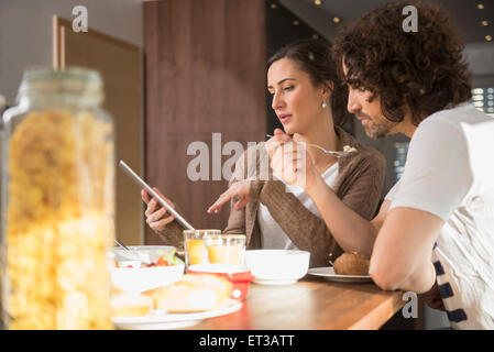 Mid adult woman using a digital tablet avec son mari pendant le petit-déjeuner, Munich, Bavière, Allemagne Banque D'Images