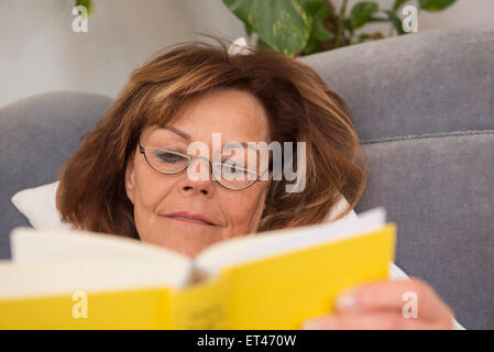 Senior woman reading a book while lying on sofa at home, Munich, Bavière, Allemagne Banque D'Images