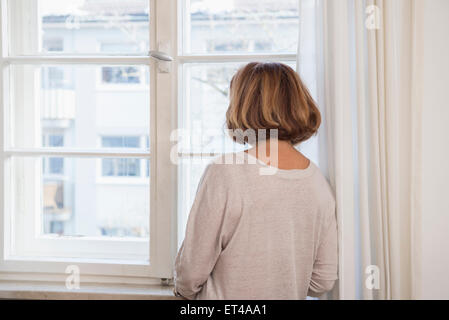 Vue arrière des hauts femme regardant à travers une fenêtre, Munich, Bavière, Allemagne Banque D'Images