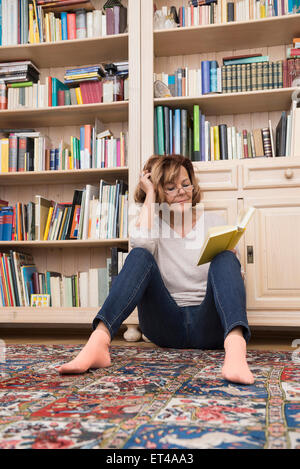 Hauts femme assise sur le sol en face de bibliothèque et de la lecture, Munich, Bavière, Allemagne Banque D'Images