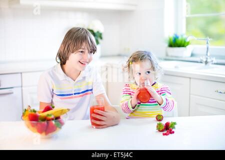 Heureux adolescent garçon et son tout-petit soeur avoir fruits et céréales pour le petit-déjeuner aux fraises avant l'école et de la maternelle Banque D'Images