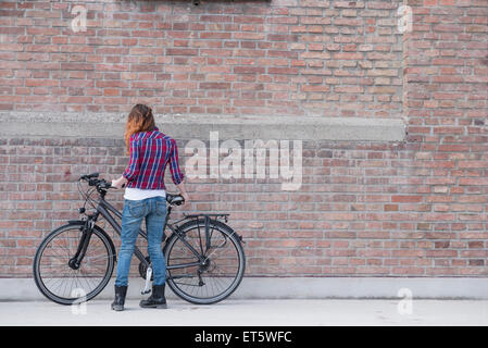 Jeune femme met location sur un mur de brique, Munich, Bavière, Allemagne Banque D'Images