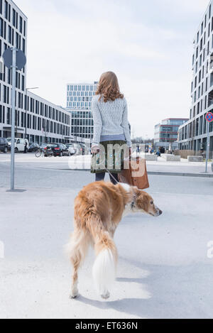 Vue arrière du femme marche sur route avec chien et valise, Munich, Bavière, Allemagne Banque D'Images
