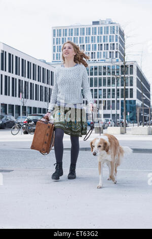 Jeune femme marche sur route avec chien et valise, Munich, Bavière, Allemagne Banque D'Images
