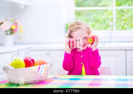 Drôle rire heureux enfant, adorable bébé fille avec des cheveux bouclés portant un chandail rose, manger des pommes rouges et vertes pour le goûter Banque D'Images