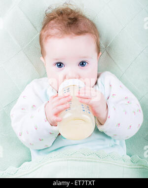 Sweet Little baby avec de beaux yeux bleus boire du lait dans une bouteille en plastique se détendre sur une couverture en tricot bleu Banque D'Images